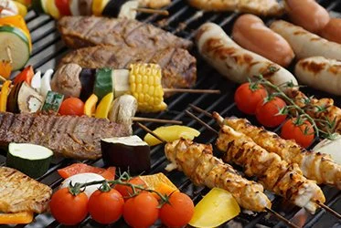 Luxe barbecue met worst, spiesen, maïs en tomaten op de grill