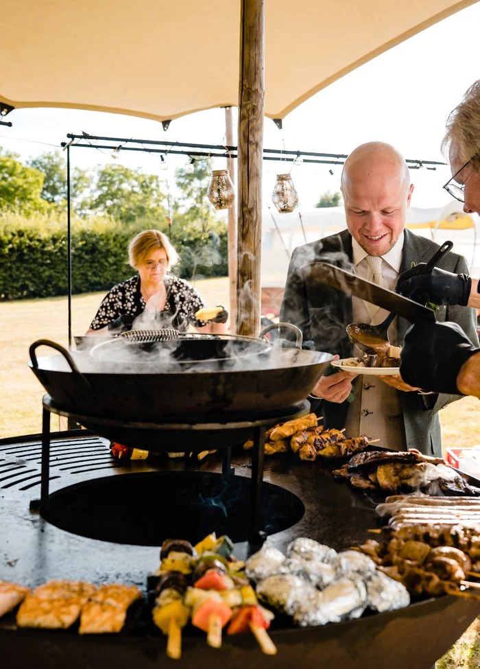 Kok bij een vuurschaal-barbecue onder een partytent