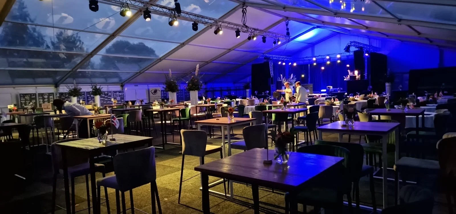 Feestzaal met statafels en blauwe podiumverlichting