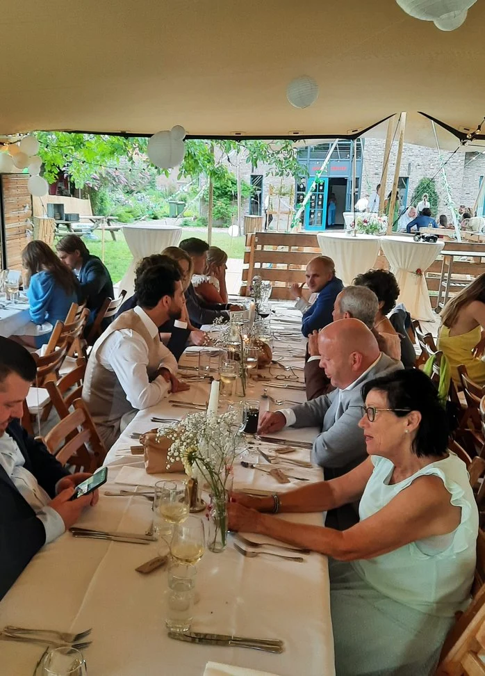 Gasten aan lange tafels onder een tent