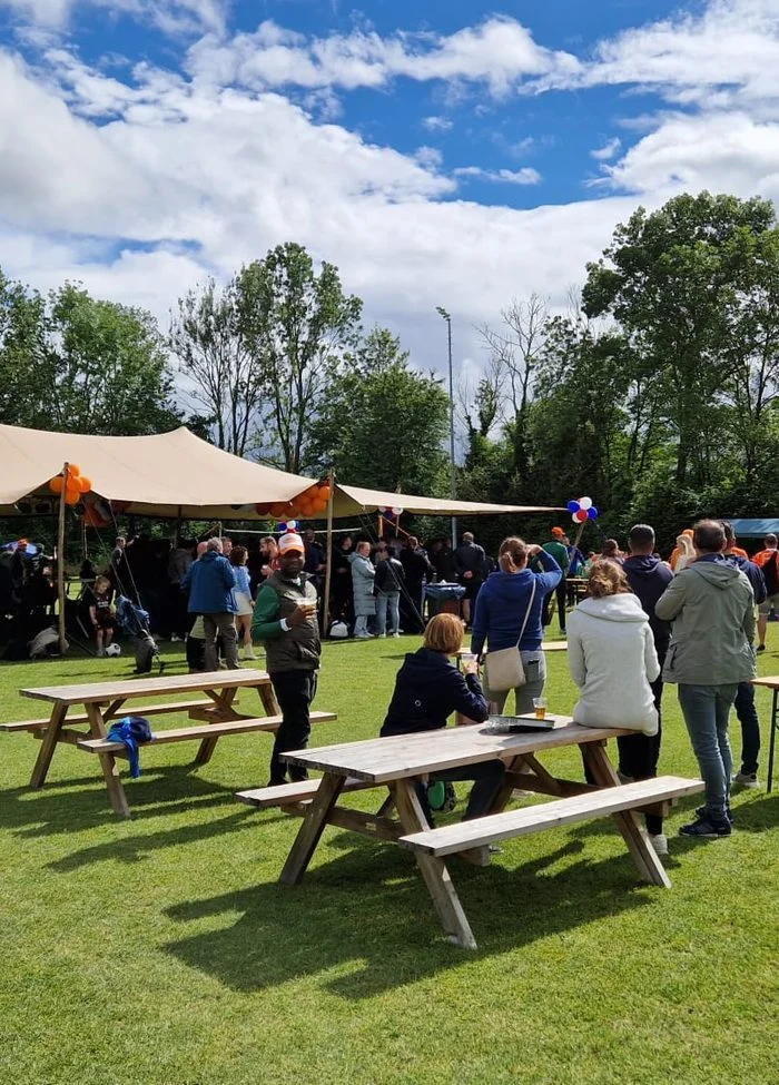Gasten bij picknicktafels onder een stretchtent